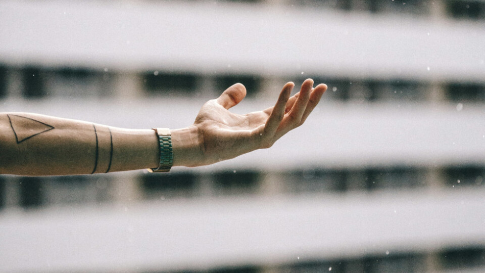 A hand raching out and catching snow with a building in the background