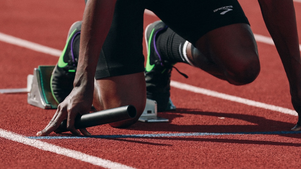 Person on the starting blocks for a running race, holding a baton.