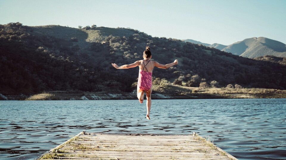 Woman jumping off a wooden pier into water