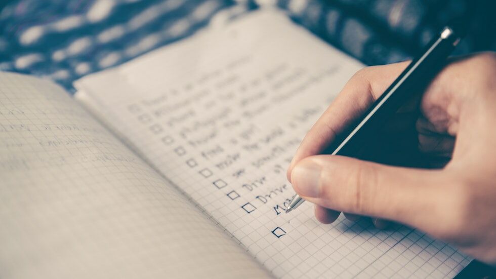 Paper notebook, showing a checklist of tasks, with a hand writing new entries