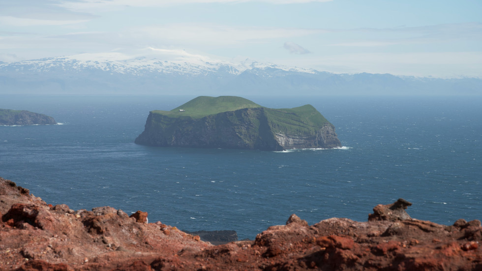 A rocky island with grass on top viewed from a distance across the water.