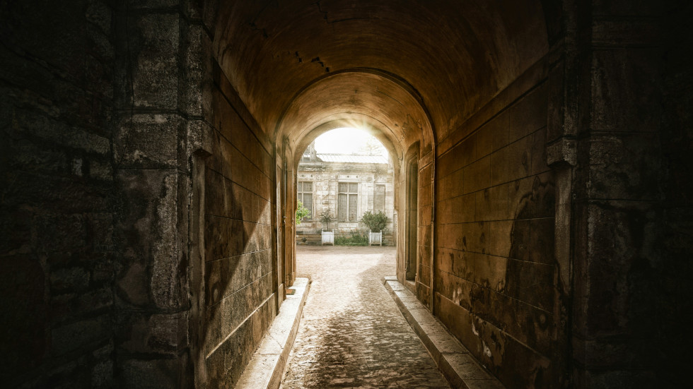 A dark tunnel looking out towards a well lit courtyard