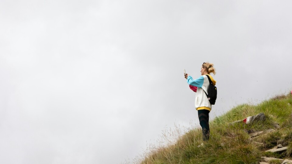 A woman on a hill, taking a picture of fog